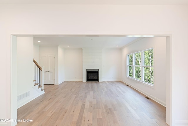 unfurnished living room with crown molding, light hardwood / wood-style flooring, and a large fireplace