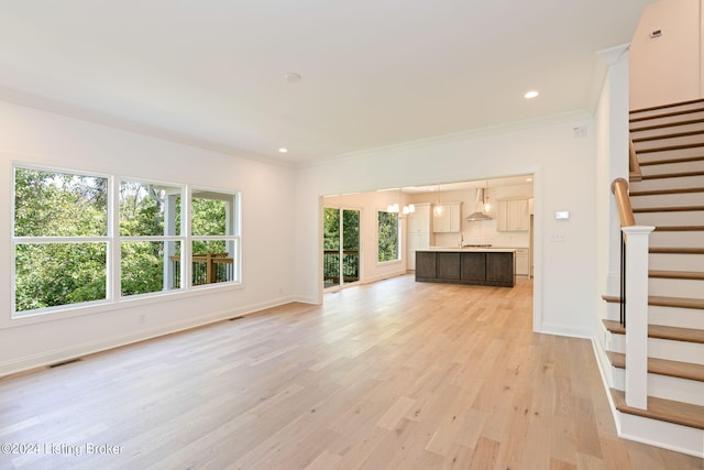 unfurnished living room featuring crown molding, an inviting chandelier, and light hardwood / wood-style floors