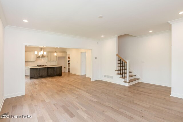 unfurnished living room featuring light wood-type flooring, ornamental molding, and a chandelier