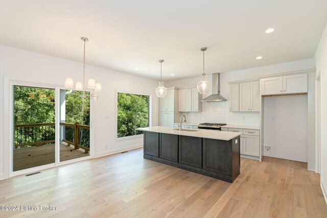 kitchen with decorative light fixtures, light hardwood / wood-style flooring, an island with sink, sink, and wall chimney range hood