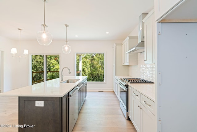 kitchen featuring decorative light fixtures, appliances with stainless steel finishes, sink, wall chimney exhaust hood, and a center island with sink