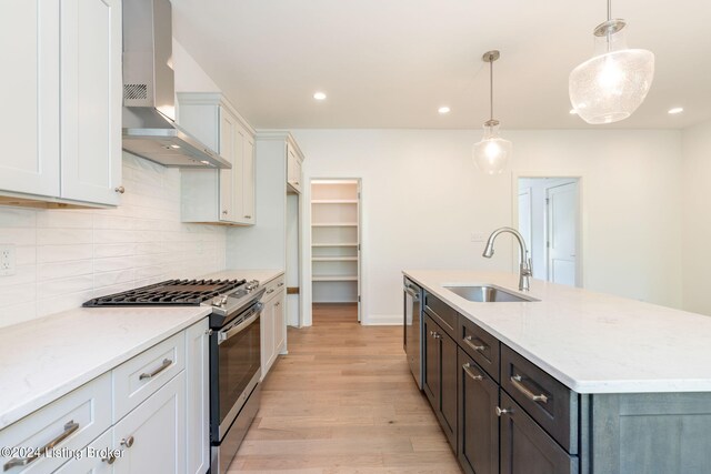 kitchen with hanging light fixtures, appliances with stainless steel finishes, sink, wall chimney exhaust hood, and a kitchen island with sink