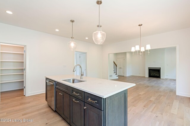 kitchen featuring light hardwood / wood-style floors, a kitchen island with sink, a large fireplace, stainless steel dishwasher, and sink