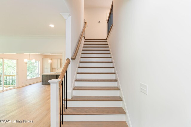 stairs with hardwood / wood-style flooring, ornamental molding, a chandelier, and sink