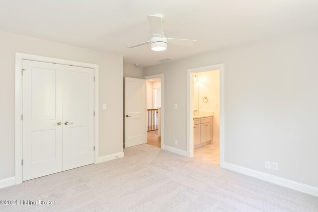 unfurnished bedroom featuring light carpet, ensuite bath, ceiling fan, and a closet