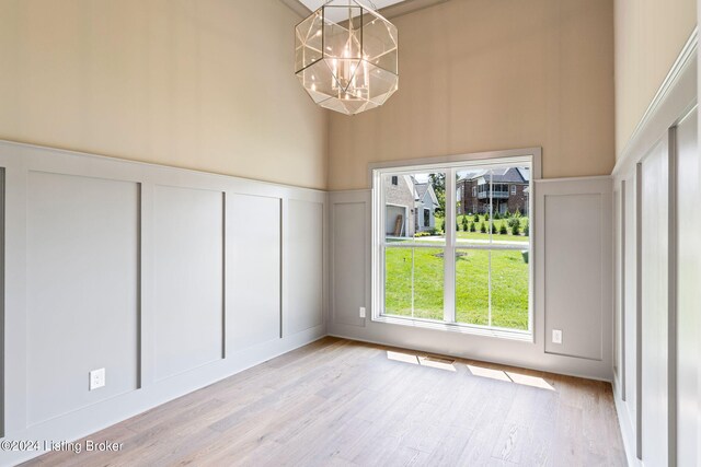 unfurnished dining area featuring light hardwood / wood-style floors, a chandelier, and a towering ceiling