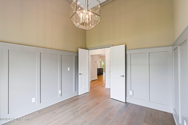 unfurnished bedroom with a towering ceiling, a notable chandelier, and light hardwood / wood-style floors