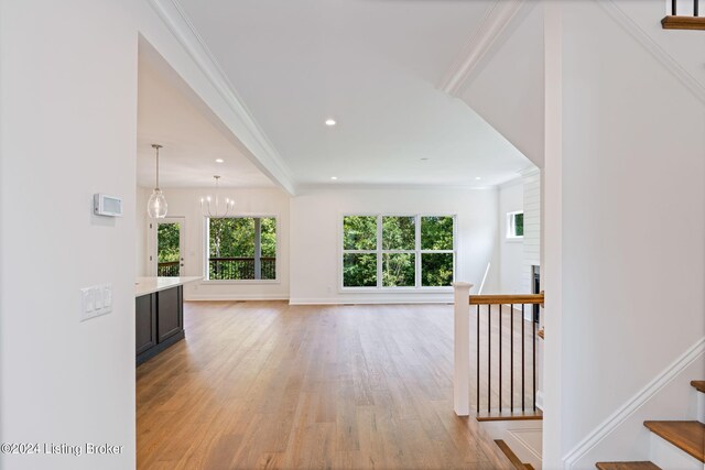 unfurnished living room with light wood-type flooring, crown molding, a fireplace, and an inviting chandelier