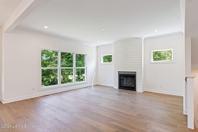 unfurnished living room with a large fireplace, plenty of natural light, light hardwood / wood-style floors, and crown molding