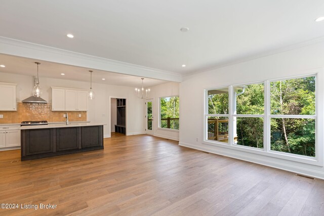 unfurnished living room with an inviting chandelier, crown molding, and light hardwood / wood-style flooring