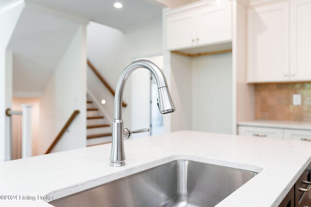 interior details with backsplash, light stone countertops, white cabinetry, and sink