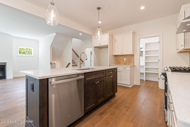 kitchen featuring a fireplace, an island with sink, stainless steel appliances, sink, and light wood-type flooring