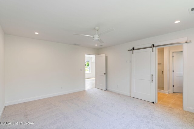 unfurnished bedroom with a barn door, ceiling fan, and light carpet