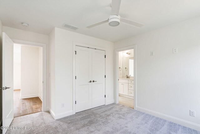 unfurnished bedroom featuring light carpet, ensuite bath, ceiling fan, and a closet