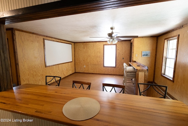 dining room with a textured ceiling, hardwood / wood-style flooring, ceiling fan, and wooden walls