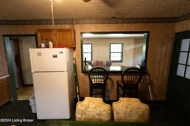 kitchen featuring a textured ceiling, a breakfast bar, kitchen peninsula, and white fridge