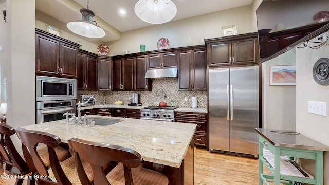 kitchen featuring dark brown cabinets, light wood-type flooring, a kitchen island with sink, sink, and appliances with stainless steel finishes