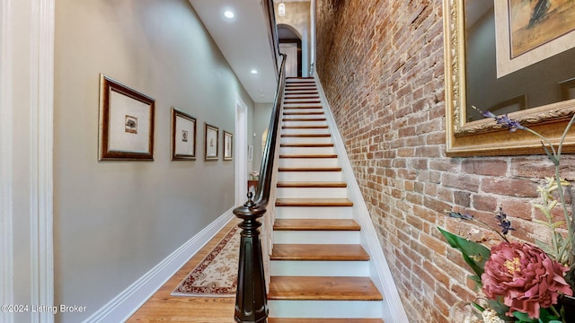 stairs with a towering ceiling, hardwood / wood-style floors, and brick wall