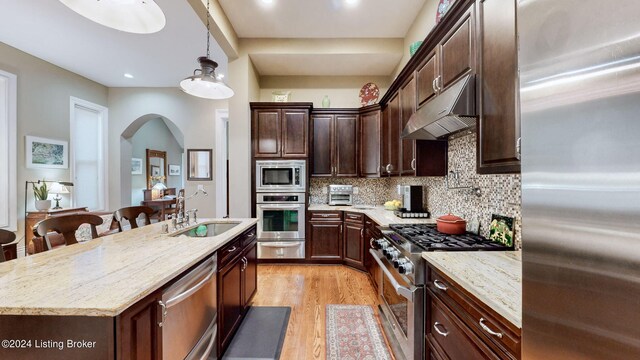 kitchen featuring hanging light fixtures, a center island with sink, appliances with stainless steel finishes, a kitchen breakfast bar, and light wood-type flooring