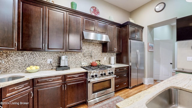 kitchen with dark brown cabinetry, light stone counters, tasteful backsplash, appliances with stainless steel finishes, and light wood-type flooring