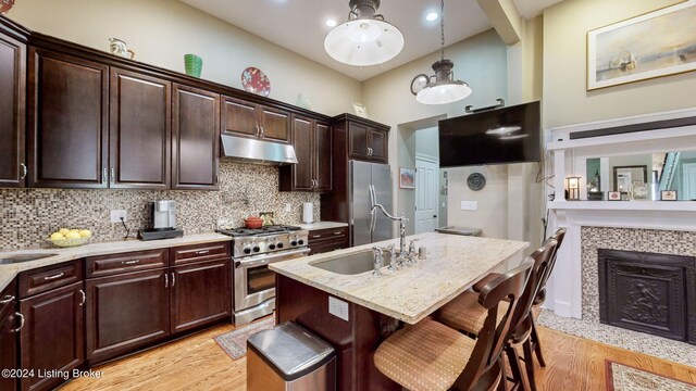 kitchen with appliances with stainless steel finishes, hanging light fixtures, a breakfast bar area, light hardwood / wood-style flooring, and a kitchen island with sink