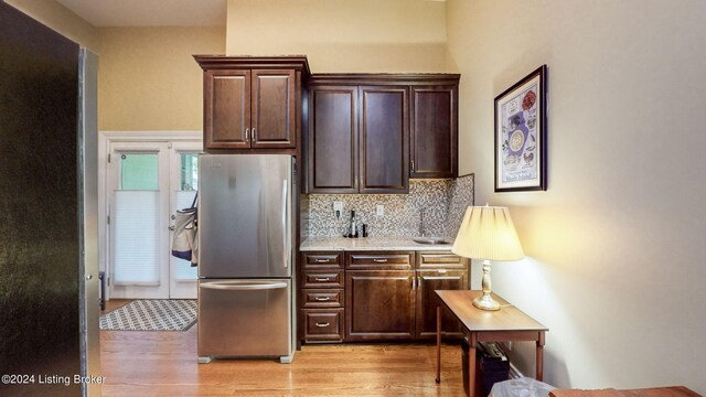 kitchen featuring dark brown cabinets, backsplash, light hardwood / wood-style flooring, and stainless steel fridge