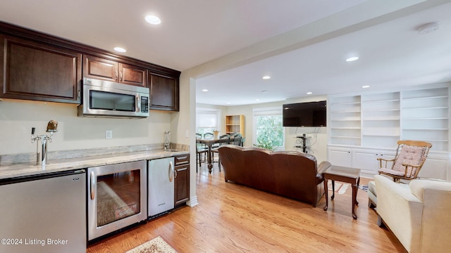 kitchen featuring dark brown cabinets, wine cooler, light hardwood / wood-style floors, stainless steel appliances, and light stone countertops