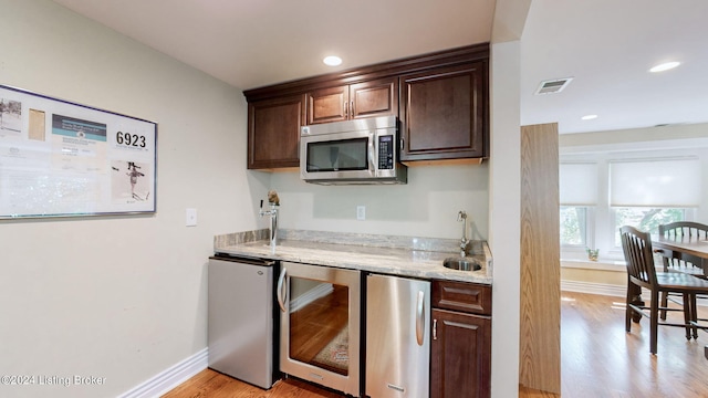 kitchen featuring dark brown cabinetry, sink, beverage cooler, appliances with stainless steel finishes, and light hardwood / wood-style floors