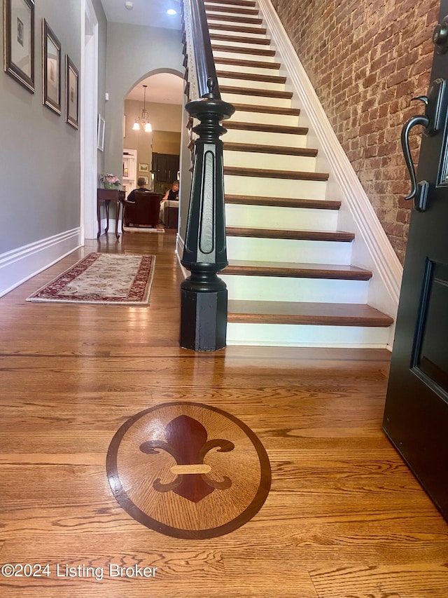 stairs with brick wall, hardwood / wood-style floors, and a high ceiling