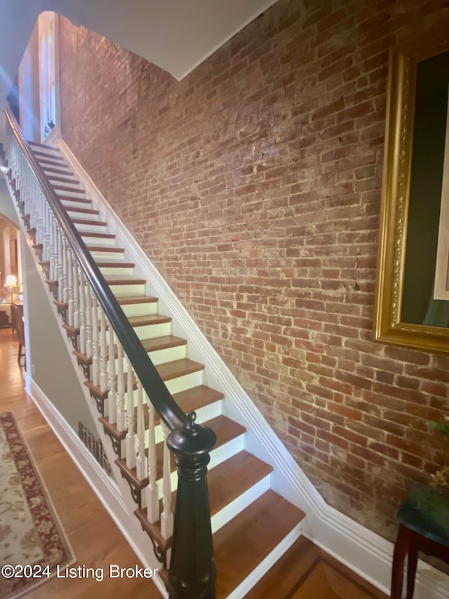 stairway with wood-type flooring and brick wall