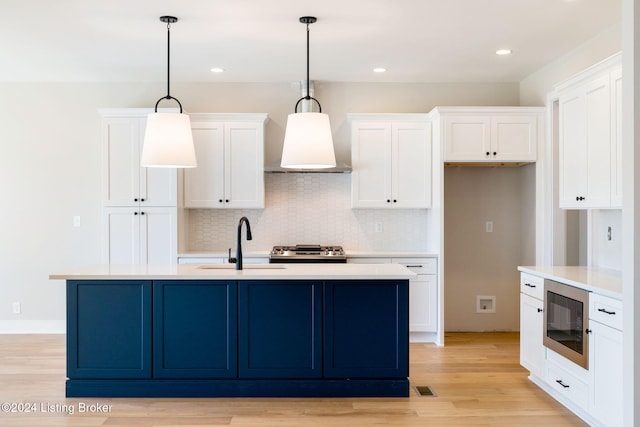 kitchen featuring light wood-type flooring, built in microwave, decorative light fixtures, stainless steel range, and a center island with sink