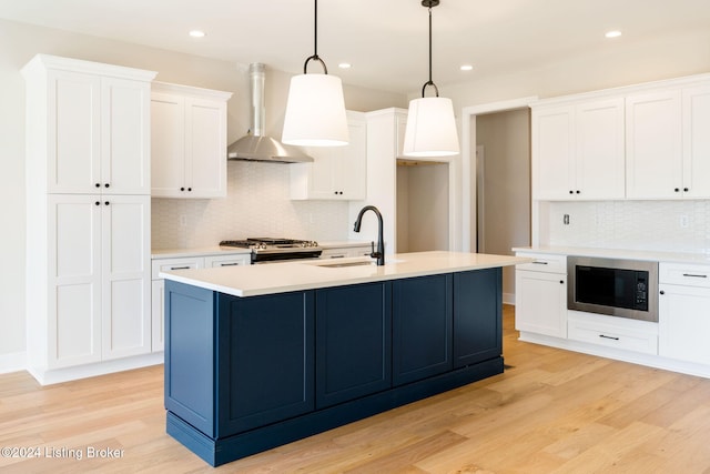 kitchen featuring sink, white cabinetry, wall chimney range hood, and pendant lighting