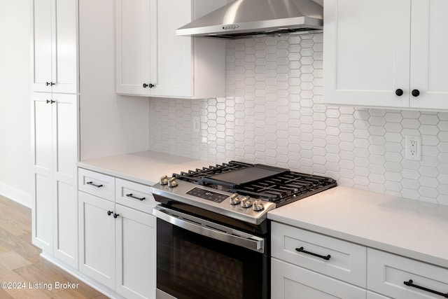 kitchen with stainless steel range with gas stovetop, light hardwood / wood-style flooring, wall chimney range hood, and backsplash