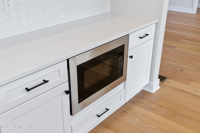 details with white cabinetry, tasteful backsplash, stainless steel microwave, and light wood-type flooring