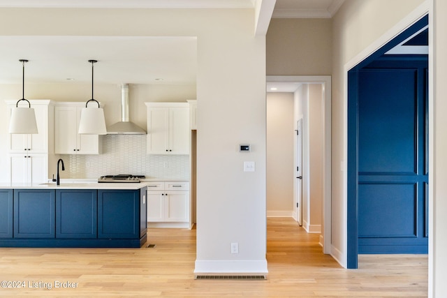 kitchen with wall chimney range hood, ornamental molding, decorative light fixtures, light wood-type flooring, and white cabinets