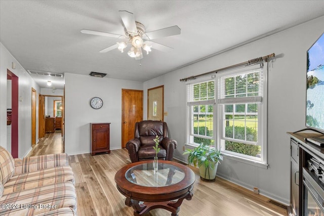 living room featuring ceiling fan, a textured ceiling, and light hardwood / wood-style flooring