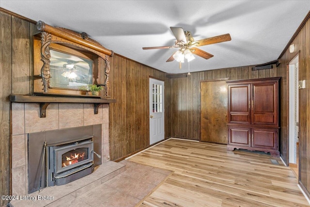 unfurnished living room with light hardwood / wood-style flooring, ceiling fan, ornamental molding, and wooden walls