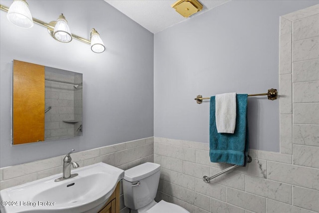 bathroom with tile walls, toilet, and vanity