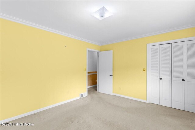 unfurnished bedroom with crown molding, light colored carpet, visible vents, and a closet