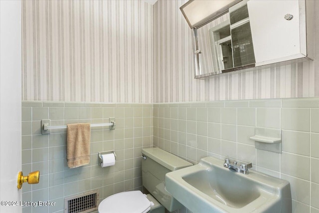 bathroom with a sink, visible vents, wainscoting, and wallpapered walls