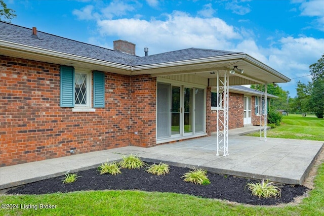 back of property featuring brick siding, a chimney, and roof with shingles