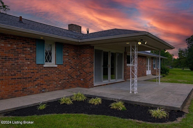 back of property at dusk with a patio, brick siding, and a chimney