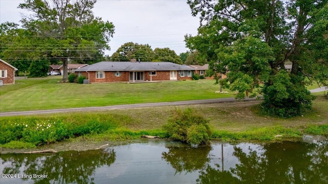 rear view of property featuring brick siding, a lawn, and a water view