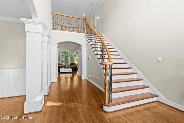 staircase with crown molding, a towering ceiling, hardwood / wood-style floors, and ornate columns