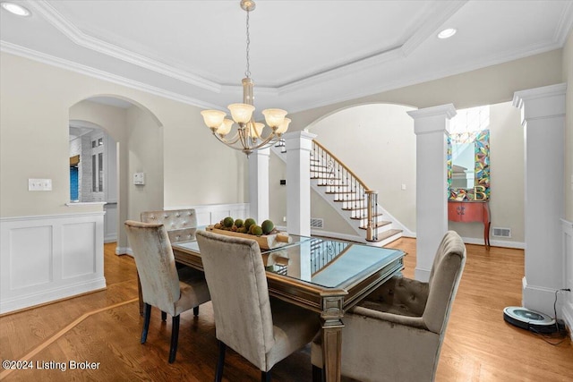 dining area featuring arched walkways, wood finished floors, a raised ceiling, and decorative columns