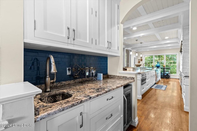 kitchen featuring beamed ceiling, beverage cooler, light wood-style flooring, a sink, and white cabinets