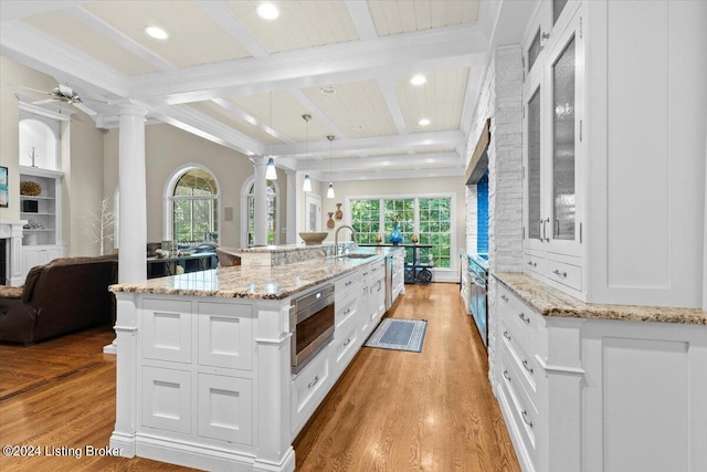 kitchen featuring a large island with sink, ornate columns, ceiling fan, and white cabinets