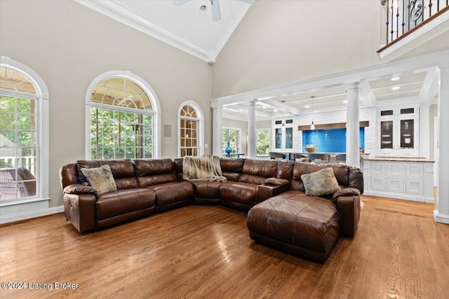 living room featuring crown molding, light hardwood / wood-style floors, ornate columns, ceiling fan, and a towering ceiling