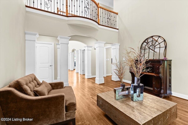 living area featuring arched walkways, baseboards, ornate columns, and wood finished floors