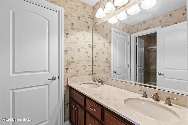 bathroom featuring double vanity, wallpapered walls, a shower, and a sink